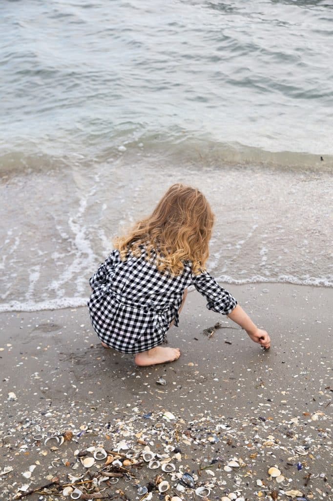 Petite fille accroupie sur une plage de sable, au bord de l'eau