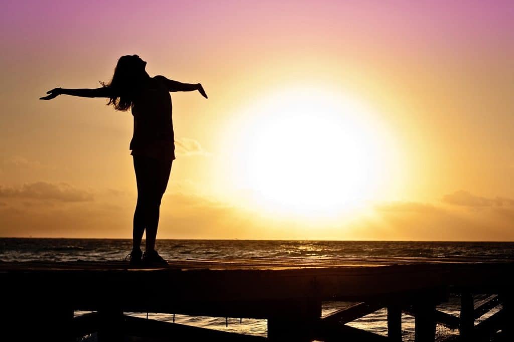 femme avec les bras ouverts, devant un coucher de soleil